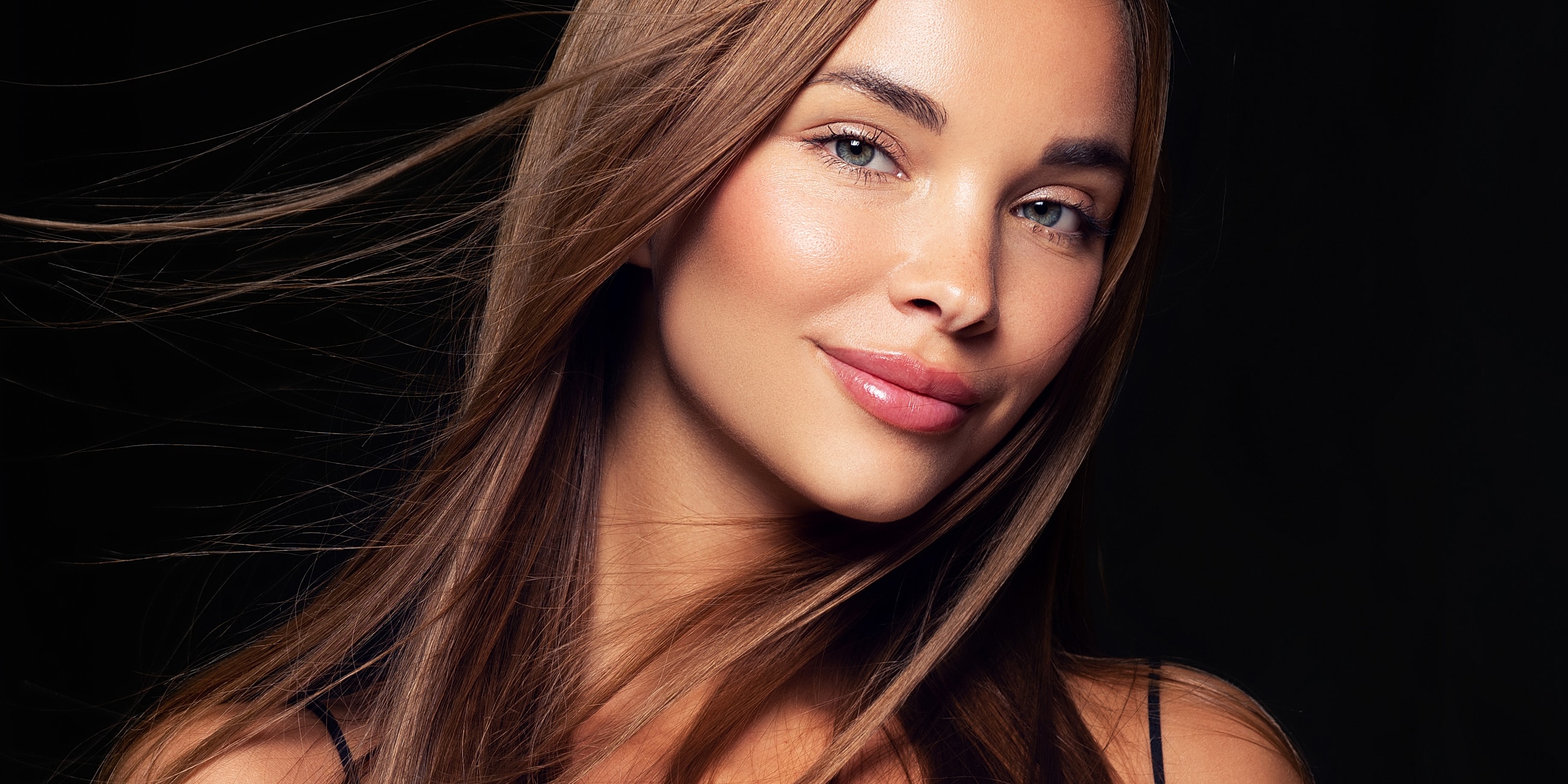 Newton under eye filler model with long hair against dark background.